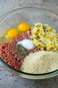 ingredients for meatballs in a glass bowl on a marble counter top, including eggs and seasoning