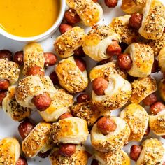 hotdogs wrapped in bread and topped with mustard on a white plate next to a bowl of dipping sauce