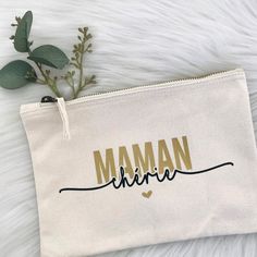 a white pouch with the word mama written in gold on it and a plant next to it