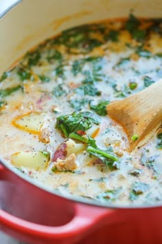 a red pot filled with broccoli, potatoes and other vegetables next to a wooden spoon