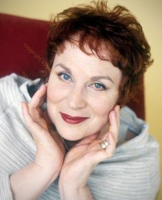 a woman with short red hair and blue eyes smiles at the camera while wearing a white sweater