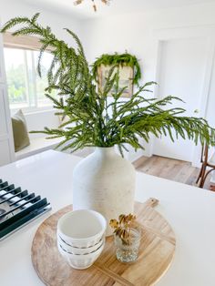 a white vase sitting on top of a wooden tray next to a bowl and plate