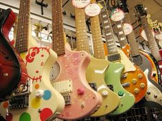 many guitars are lined up on display in a room with hello kitty signs hanging from the ceiling