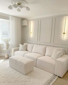 a living room with a large white couch and ottoman in front of a window on the wall