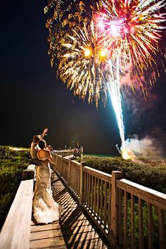 a bride and groom standing on a bridge with fireworks in the background