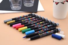 several markers are lined up on a table next to two cups and a pencil holder