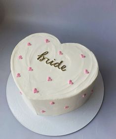 a white heart shaped cake with pink hearts on it and the word bride written in gold