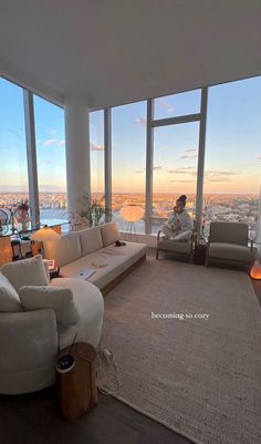 a man sitting on a couch in a living room with large windows overlooking the city