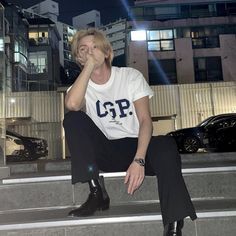 a woman sitting on the steps in front of a building at night with her hand to her face