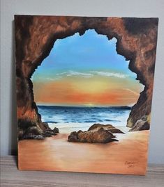 a painting of an ocean cave with the sun setting in the distance and rocks on the beach