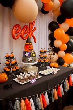 a table topped with cupcakes and desserts covered in orange and black balloons