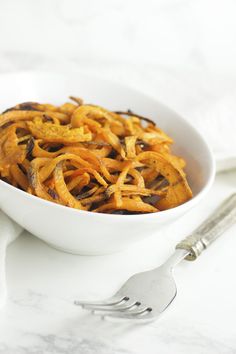 a white bowl filled with cooked food next to a fork and knife on a table