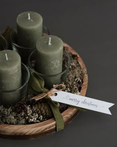 four candles are sitting in a bowl with moss and pine cones around it, tied with a ribbon