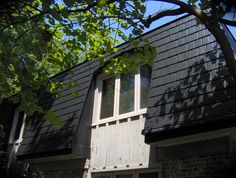 a house with black shingles and white shutters on the windows is seen through some trees