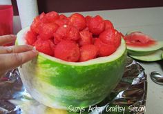 a person is holding up a watermelon bowl with strawberries in it