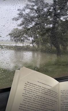 an open book sitting on top of a window sill next to a rain covered street