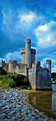 an old castle sitting on top of a rocky shore next to the ocean under a cloudy blue sky