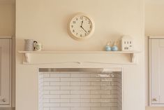 a clock mounted on the wall above a fireplace in a living room with white cabinets