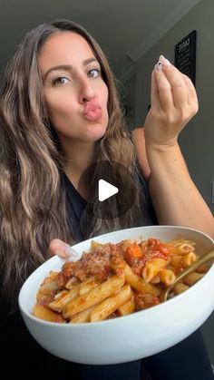 a woman making a funny face while holding a bowl of pasta in front of her