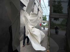 a man walking down a street next to a tall white sculpture on the side of a building