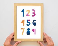 two hands holding up a framed art print with numbers on the front and back sides