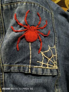 a red spider embroidered on the back of a jean jacket with webs in it