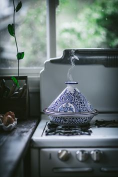 a blue and white tea pot sitting on top of a stove next to a window