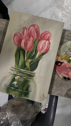 a painting of pink tulips in a mason jar on a table next to an easel