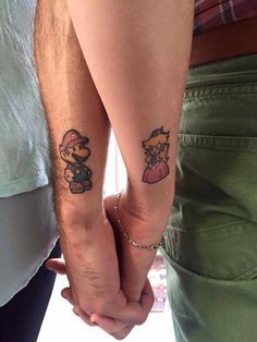 two people holding hands with small tattoos on their arms, one has a mario and luigi