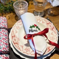 the napkins are wrapped in red ribbon and placed on top of white plates with holly designs