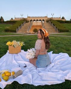 a woman sitting on top of a blanket next to a basket of flowers and lemons