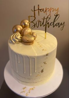 a white birthday cake with gold decorations and a happy birthday sign