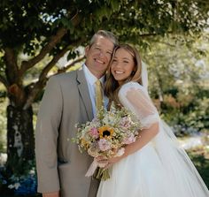 a bride and groom pose for a photo in front of a tree at their wedding