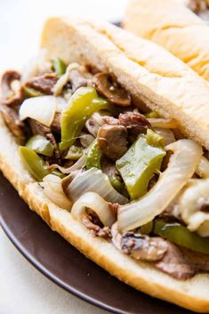 two hot dogs with onions, peppers and mushrooms on a plate in front of another sandwich