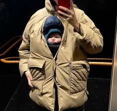 a woman taking a selfie with her baby in a stroller jacket and hat