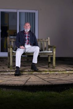 an older man sitting on a wooden bench in front of a building with sliding glass doors