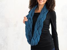 a woman with curly hair wearing a blue scarf and black shirt standing in front of a white wall