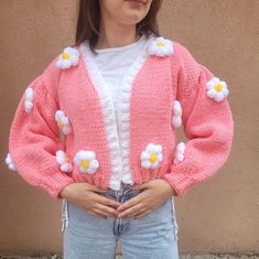 a woman standing in front of a wall wearing a pink cardigan with flowers on it