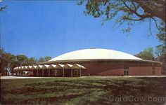 a large building sitting on top of a lush green field next to a forest filled with trees