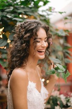 a woman in a white dress smiles and holds a green plant with leaves on it