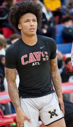 a young man with an afro standing in front of a basketball court wearing shorts and a t - shirt