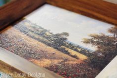 an oil painting of a field with trees and flowers in the foreground is framed