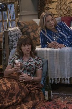 two women are sitting on the couch drinking wine