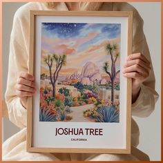 a woman holding up a framed poster with the name joshua tree in front of her