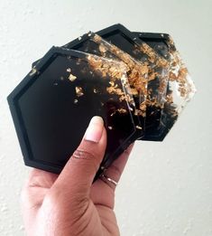 a hand holding three pieces of black and gold foiled paper on top of each other