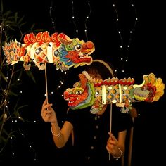 a woman holding two dragon shaped paper umbrellas in front of a tree with lights on it