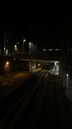 a train station at night with the lights on and tracks running parallel to each other