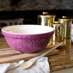 a pink bowl sitting on top of a wooden cutting board next to two gold cups