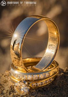 two wedding rings sitting on top of each other in the sand with their reflection in them