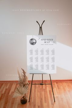 a white sign sitting on top of a wooden floor next to a vase filled with flowers